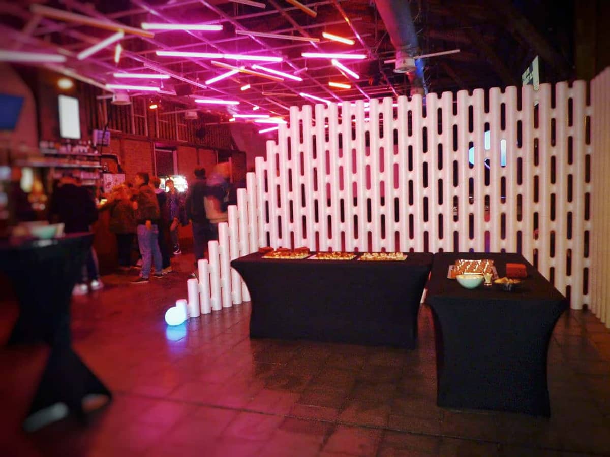 Stepped white partition wall dividing a catering area in a large event hall with pink lighting