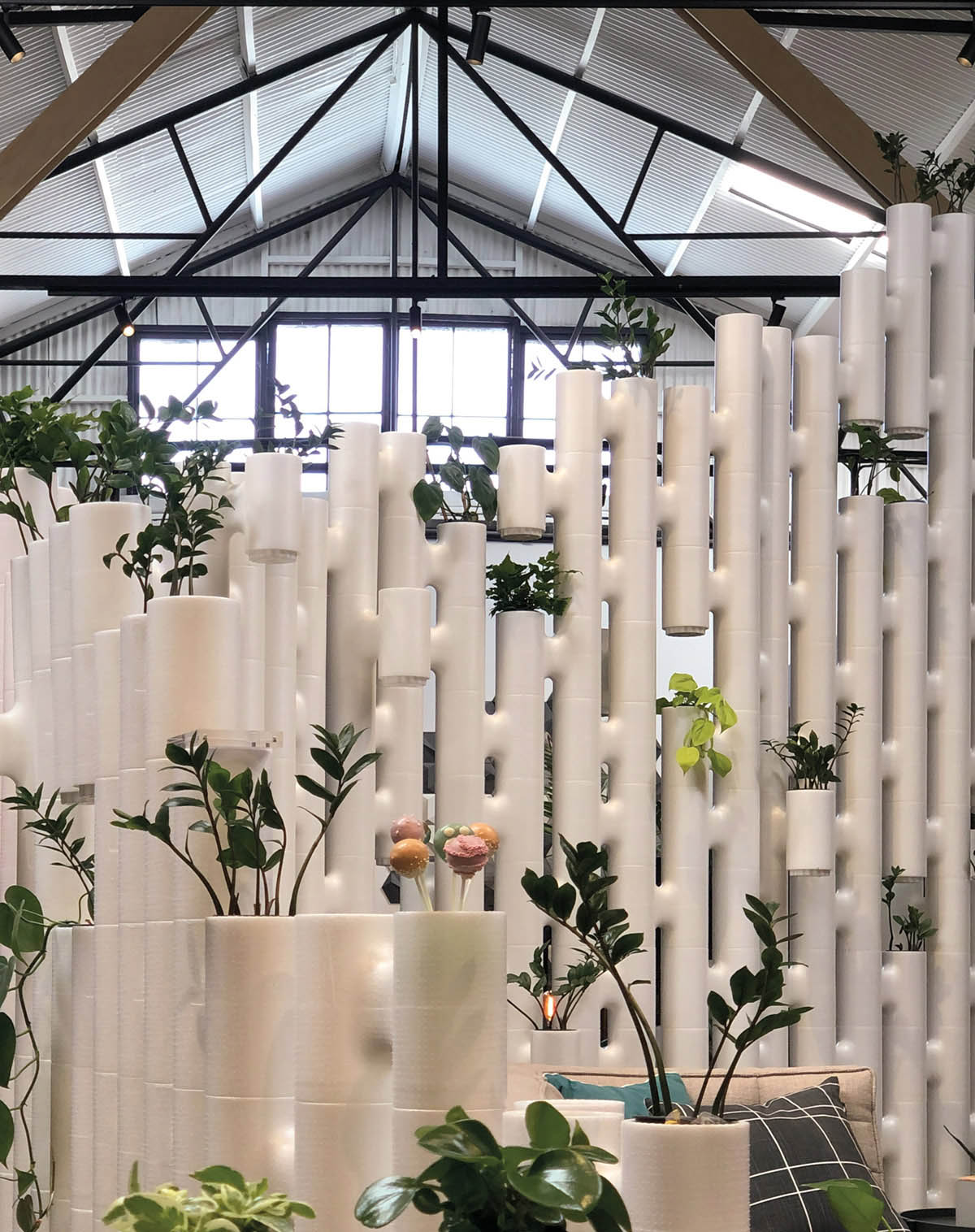 Tall white modular partition wall with plants growing out of the units in an industrial hall