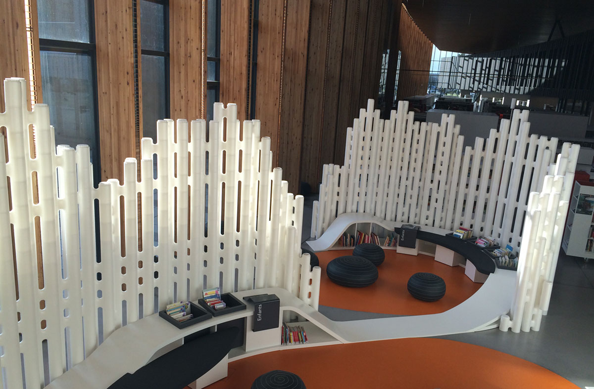 Curved white room dividers framing a reading area with an orange floor at Saint-Malo Mediatheque